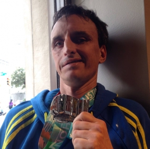 Close up of a smiling man holding a brightly colored Austin Marathon medal up near his face.
