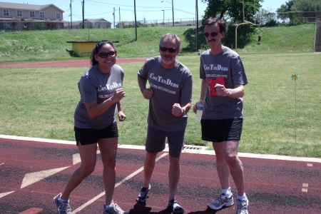Three people in matching running shirts pose on an outdoor track.