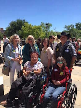 Under a bright blue sky, a group of people pose for a photo. Four stand behind two seated in wheelchairs.