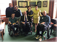 A group of people in business dress gather for a photo, some in wheelchairs, others standing.