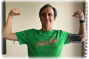 A grinning William holds up his arms to flex his biceps. He's wearing a green running shirt and arm band that holds his phone.