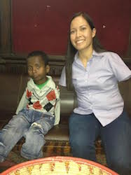 A young boy and a woman, Jessica Cox, both without arms, sit on a black bench. She smiles readily at the camera, his expression is more hesitant.
