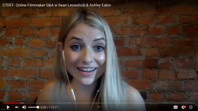 Screen shot of YouTube video, Ashley wearing earbuds, looking into the camera with raised eyebrows and a smile.