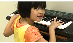 A girl playing the keyboard looks over her shoulder and smiles toward the camera