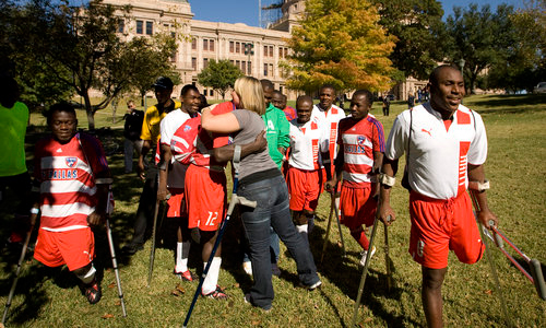 soccer player with a crutch on his arm hugs a woman, in the middle of a group of players with various amputations