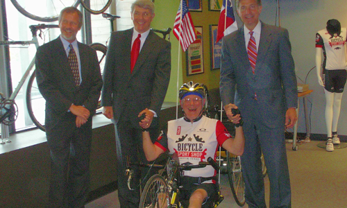 Three men in suits, one male hand-cyclist
