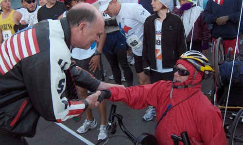 A man bends down to shake hands with hand-cyclist